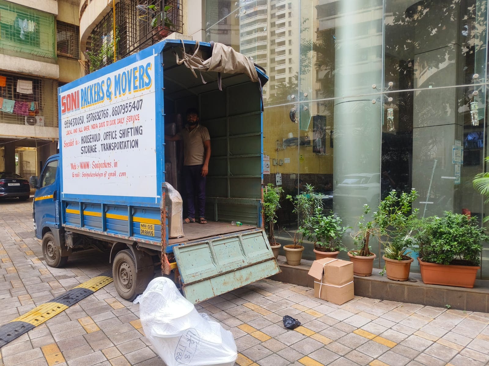 Soni Packers moving truck with a crew member and wrapped goods outside a commercial building