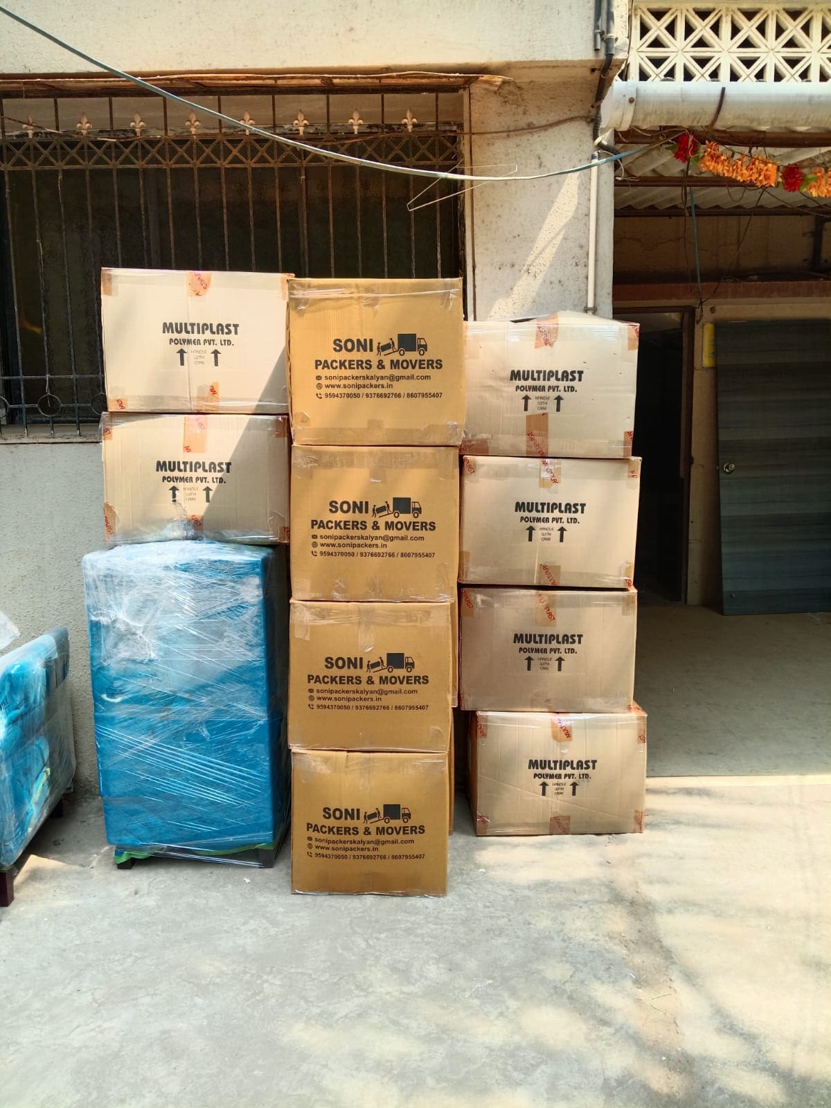 Stack of Soni Packers branded cartons and a wrapped item outside a building