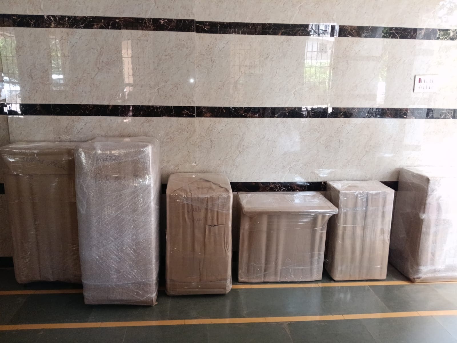 Row of wrapped furniture pieces standing against a wall ready for loading