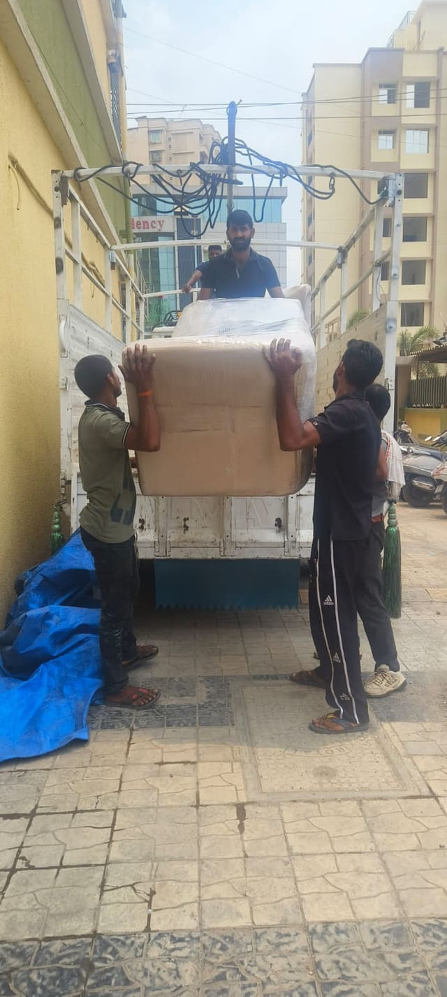 Crew members carrying a large wrapped item towards a loading vehicle