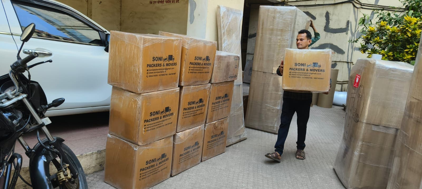 Crew member carrying a packed carton beside wrapped household goods during a move