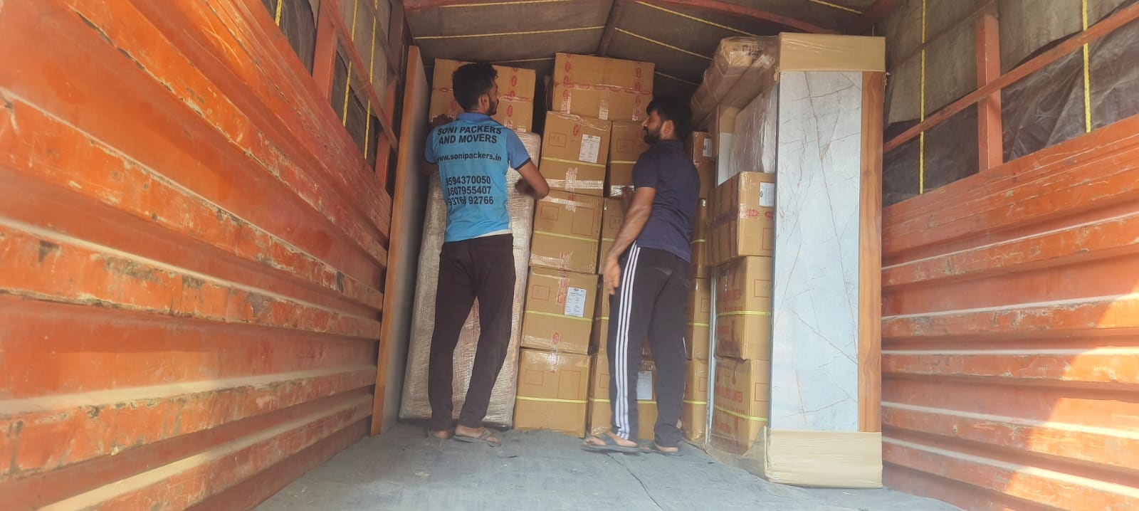 Two crew members stacking packed cartons inside a transport container