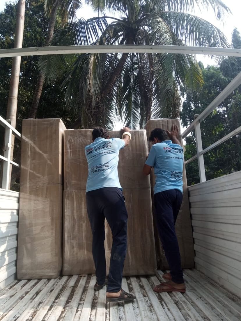 Two uniformed crew members lifting a wrapped item into the back of a moving truck