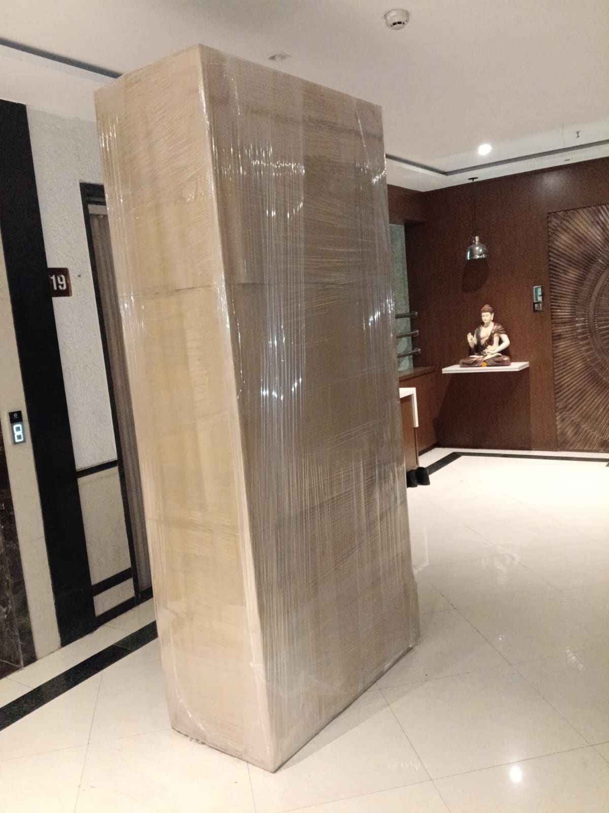 Tall wrapped wardrobe standing in a building corridor during a move